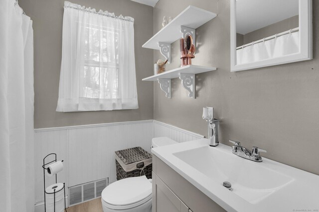 full bathroom featuring a wainscoted wall, visible vents, vanity, and toilet