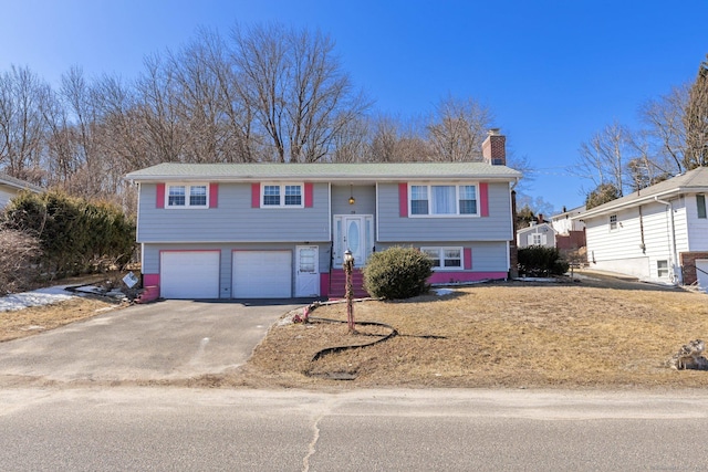 bi-level home with aphalt driveway, a chimney, and an attached garage