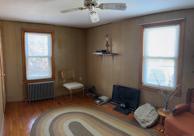 interior space with a ceiling fan, wooden walls, radiator, and wood finished floors