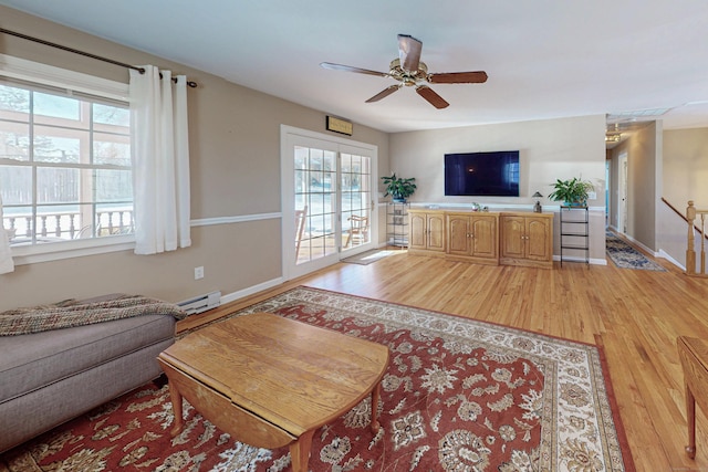 living room featuring a baseboard heating unit, light wood finished floors, a ceiling fan, and baseboards