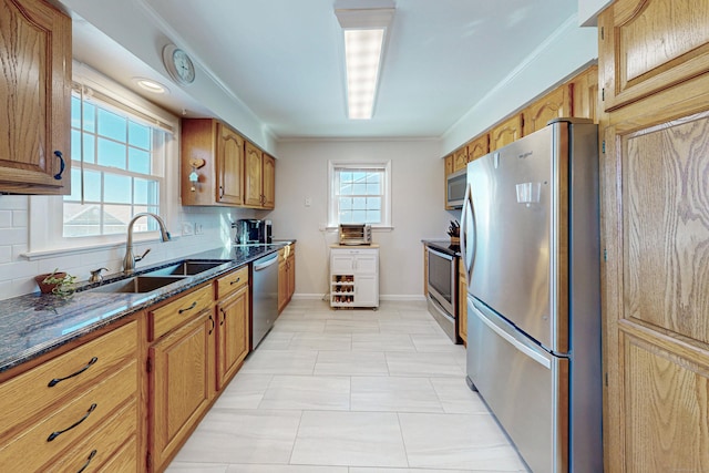 kitchen with stainless steel appliances, a sink, backsplash, dark stone counters, and brown cabinetry