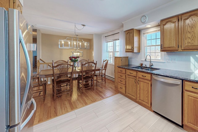 kitchen featuring dark stone counters, appliances with stainless steel finishes, brown cabinets, pendant lighting, and a sink