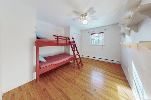 bedroom featuring baseboards, a ceiling fan, wood finished floors, a baseboard heating unit, and a closet