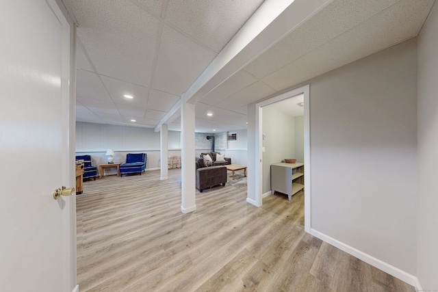 finished below grade area featuring a paneled ceiling, baseboards, light wood finished floors, and recessed lighting