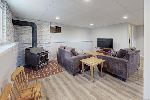 living area with wood finished floors, a wood stove, an AC wall unit, a paneled ceiling, and recessed lighting