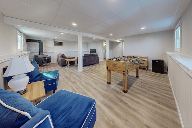 game room with a wood stove, light wood-type flooring, a paneled ceiling, and recessed lighting