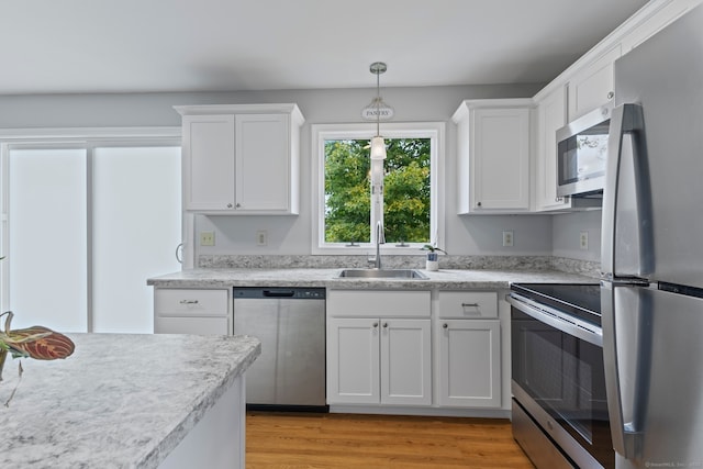 kitchen with appliances with stainless steel finishes, light hardwood / wood-style flooring, white cabinets, decorative light fixtures, and sink