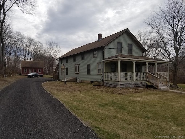 exterior space featuring covered porch, aphalt driveway, a chimney, and a lawn