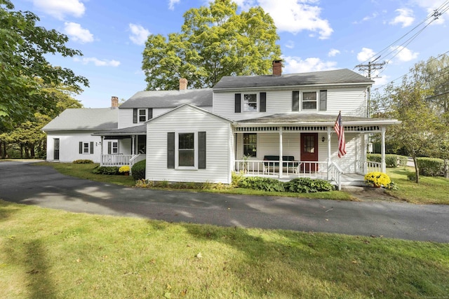 view of front of property featuring covered porch, a chimney, and a front yard