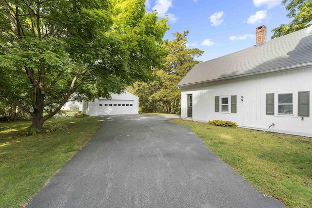 view of property exterior featuring a garage, a chimney, a lawn, and an outdoor structure