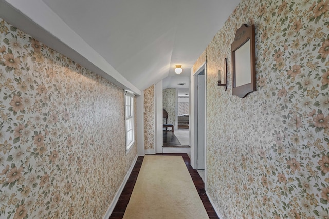 hall featuring dark wood-style floors, vaulted ceiling, and wallpapered walls