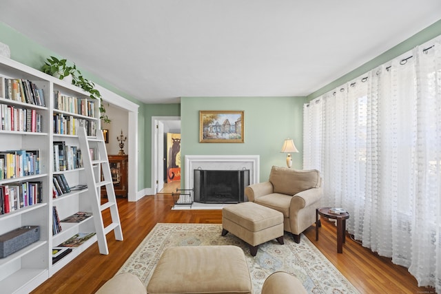 sitting room with a fireplace with raised hearth and wood finished floors