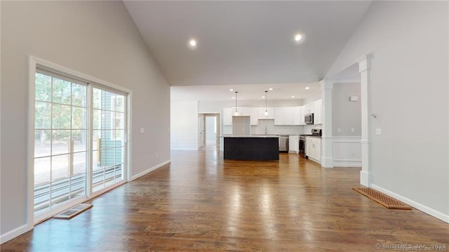 unfurnished living room with dark wood-style flooring, high vaulted ceiling, baseboards, and decorative columns