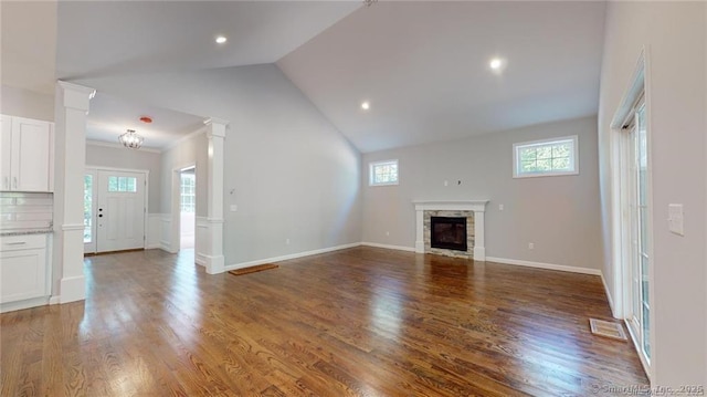 unfurnished living room with visible vents, wood finished floors, a stone fireplace, baseboards, and ornate columns