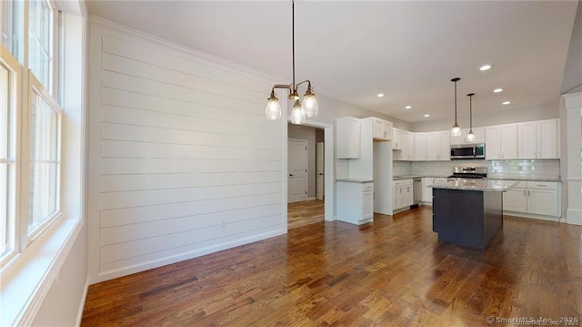 kitchen featuring tasteful backsplash, stainless steel microwave, range, white cabinetry, and dark wood-style flooring