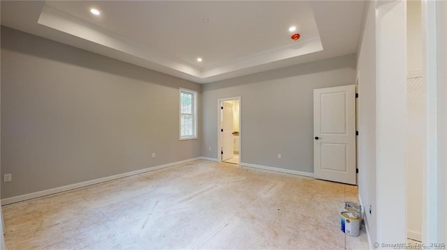 unfurnished bedroom with recessed lighting, a tray ceiling, baseboards, and ensuite bath