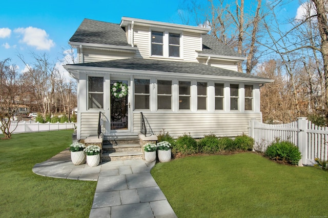 traditional style home featuring a front lawn, a shingled roof, and fence