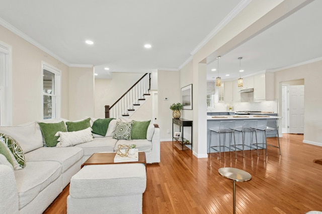 living area with ornamental molding, stairway, light wood-style flooring, and baseboards