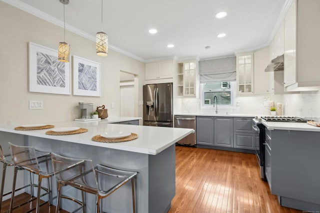 kitchen featuring crown molding, gray cabinetry, appliances with stainless steel finishes, a peninsula, and wall chimney exhaust hood