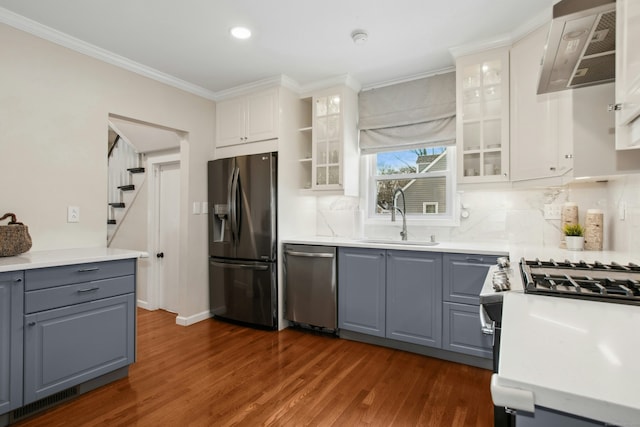 kitchen with dark wood finished floors, appliances with stainless steel finishes, ornamental molding, white cabinetry, and a sink