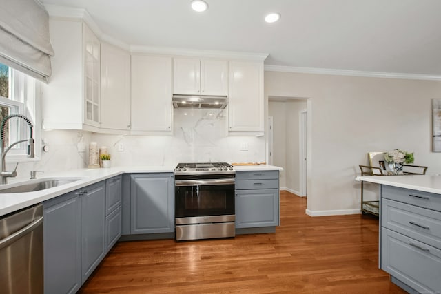 kitchen with stainless steel appliances, gray cabinetry, ornamental molding, a sink, and under cabinet range hood