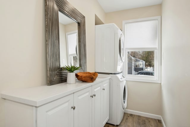 washroom featuring stacked washer and dryer, cabinet space, baseboards, and a wealth of natural light