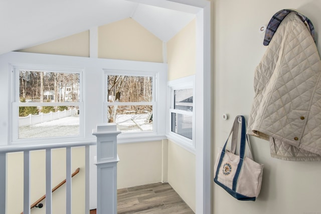 hallway featuring vaulted ceiling, an upstairs landing, and light wood-style floors