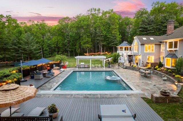 16 Whitehall Pl, Farmington, CT 06032 - pool at dusk with a wooden deck, a pergola, outdoor dining space, an outdoor living space with a fire pit, and a pool with connected hot tub
