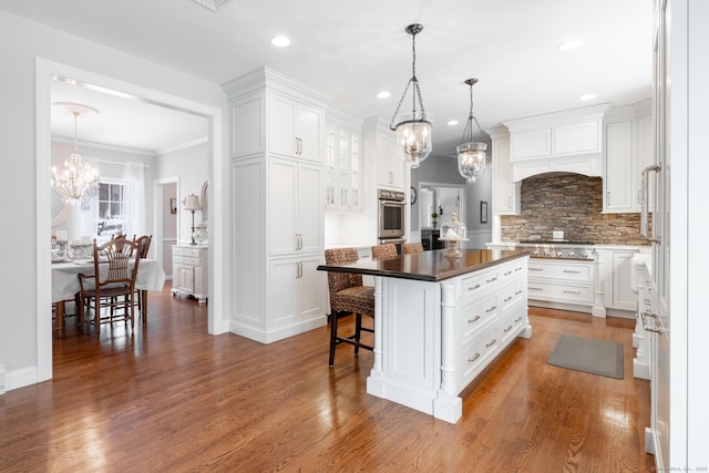 kitchen with a notable chandelier, wood finished floors, a kitchen island, white cabinets, and backsplash