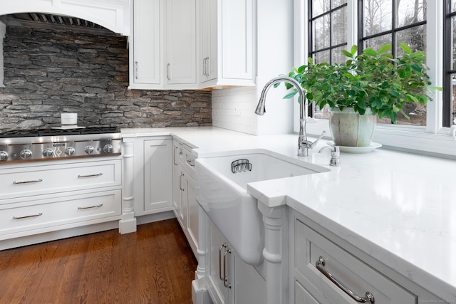 kitchen with stainless steel gas cooktop, a sink, white cabinets, tasteful backsplash, and dark wood finished floors