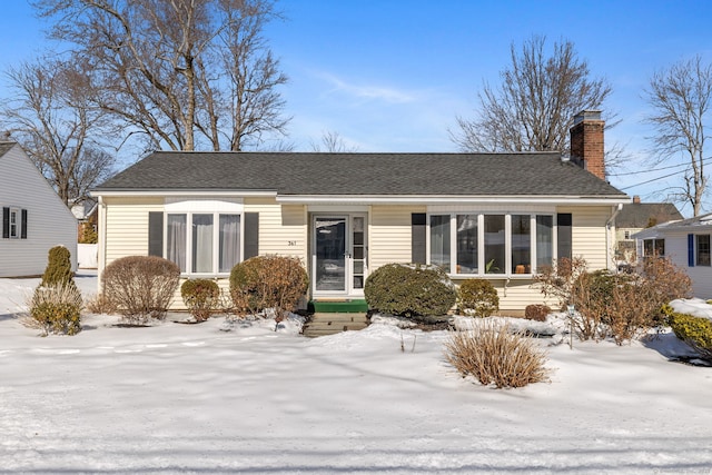 snow covered rear of property featuring a shingled roof and a chimney