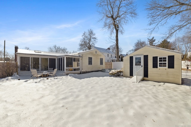 snow covered house featuring a sunroom, fence, and a fire pit