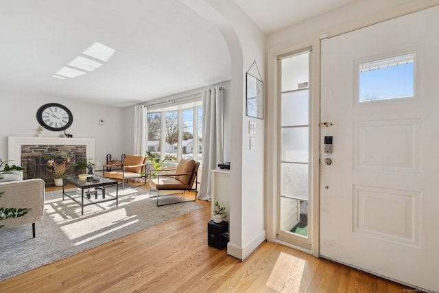 entryway with arched walkways, a stone fireplace, light wood-style flooring, and baseboards