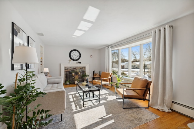 living area featuring visible vents, a baseboard radiator, a fireplace, and light wood-style flooring