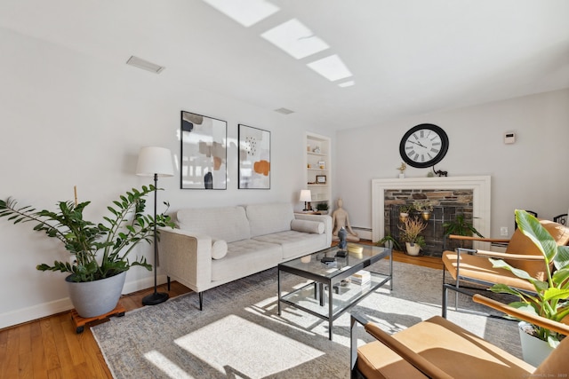 living room with built in shelves, a fireplace, visible vents, wood finished floors, and baseboards