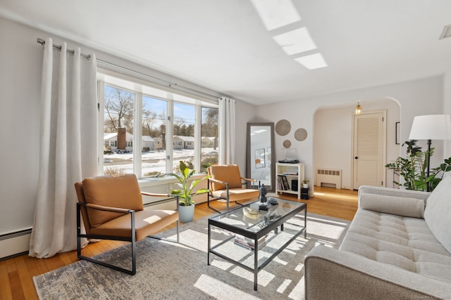 living room featuring light wood-type flooring, arched walkways, radiator, and visible vents