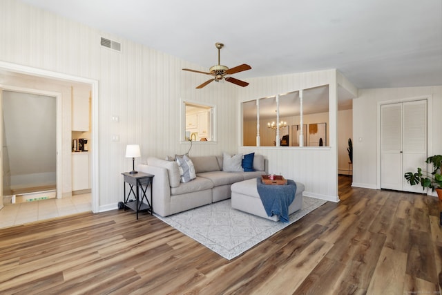 living area featuring ceiling fan with notable chandelier, wood finished floors, visible vents, baseboards, and baseboard heating