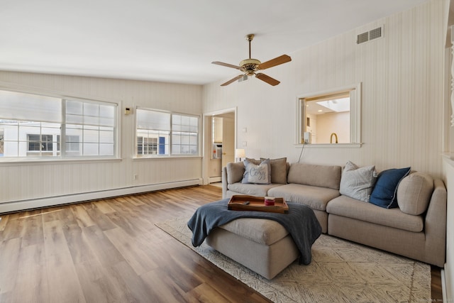 living area with a baseboard heating unit, light wood-type flooring, visible vents, and a ceiling fan