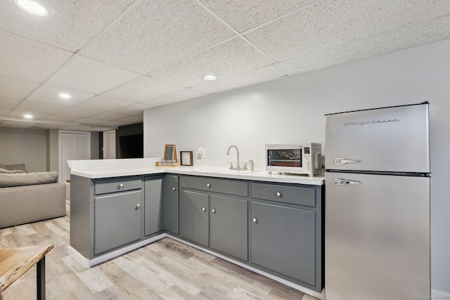 kitchen with light countertops, freestanding refrigerator, open floor plan, a sink, and a peninsula