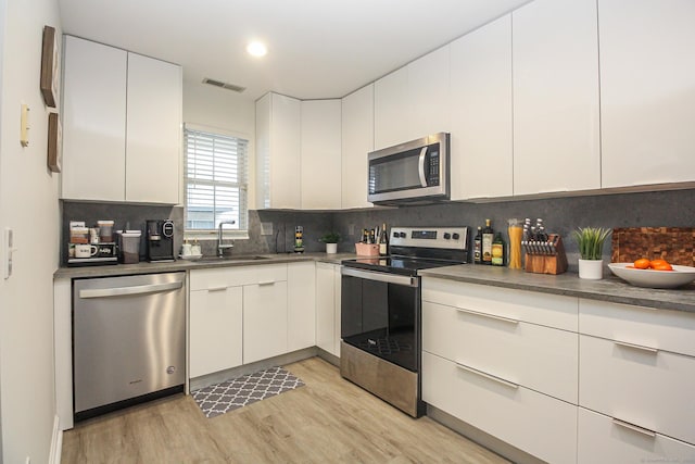 kitchen featuring light hardwood / wood-style flooring, sink, white cabinetry, stainless steel appliances, and tasteful backsplash