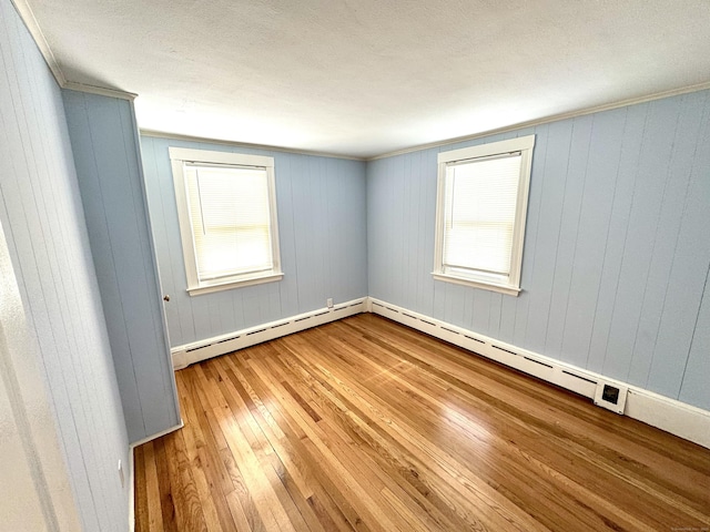 empty room featuring ornamental molding, a baseboard radiator, a healthy amount of sunlight, and wood finished floors