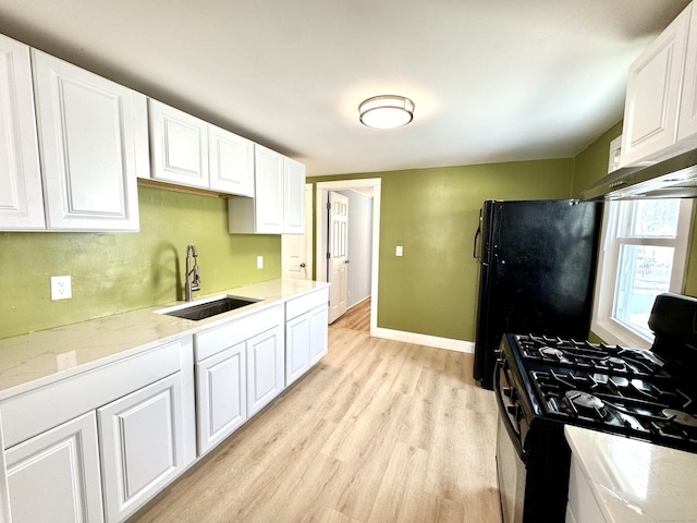 kitchen with a sink, white cabinetry, baseboards, light wood-style floors, and black appliances