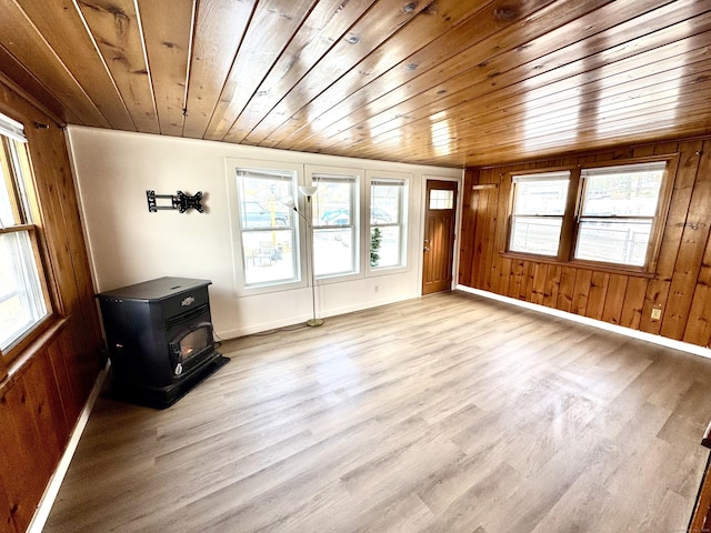 unfurnished living room featuring a wood stove, wood walls, light wood-type flooring, and wooden ceiling