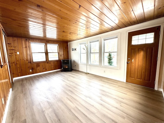 unfurnished living room featuring wood walls, wood ceiling, baseboards, light wood-style floors, and a wood stove