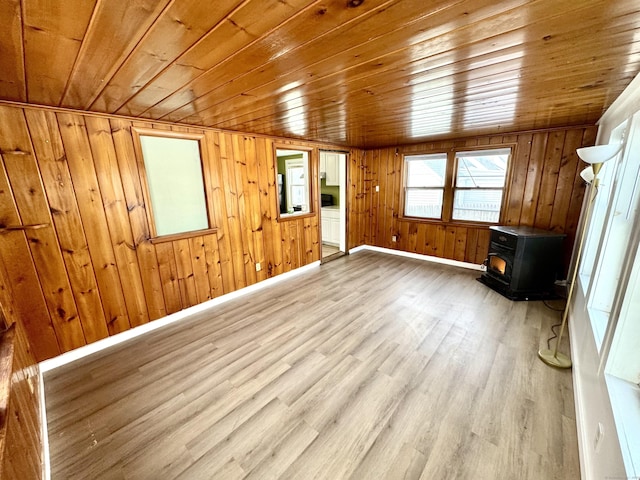 unfurnished living room with a wood stove, wooden ceiling, baseboards, and wood finished floors