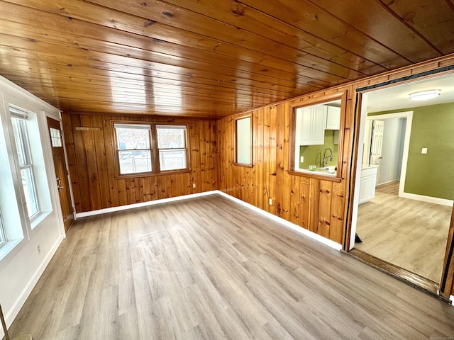 unfurnished room featuring wooden walls, light wood finished floors, wood ceiling, and baseboards