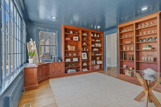 sitting room with radiator, light wood-style flooring, visible vents, and ornamental molding