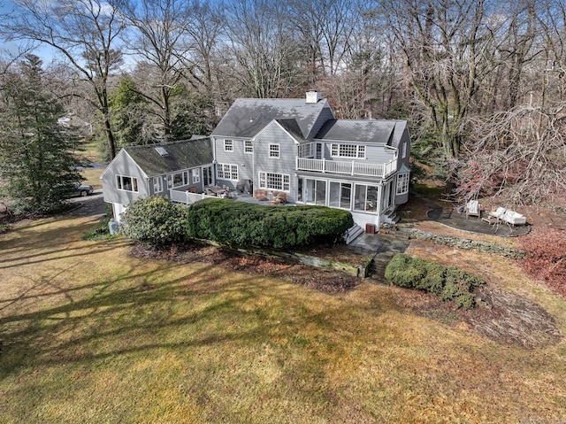 view of front of home with a sunroom, a front yard, a chimney, and a balcony