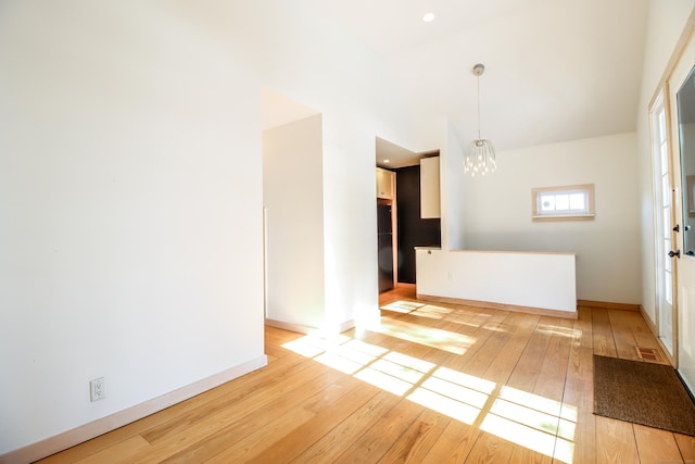 spare room with light wood-style flooring, a chandelier, and baseboards