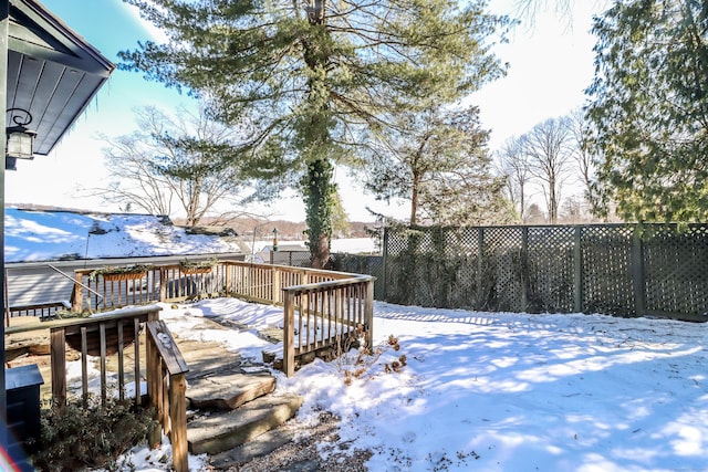 yard covered in snow with a wooden deck and fence